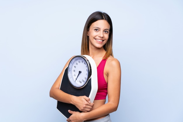 Young sport woman over isolated blue  with weighing machine