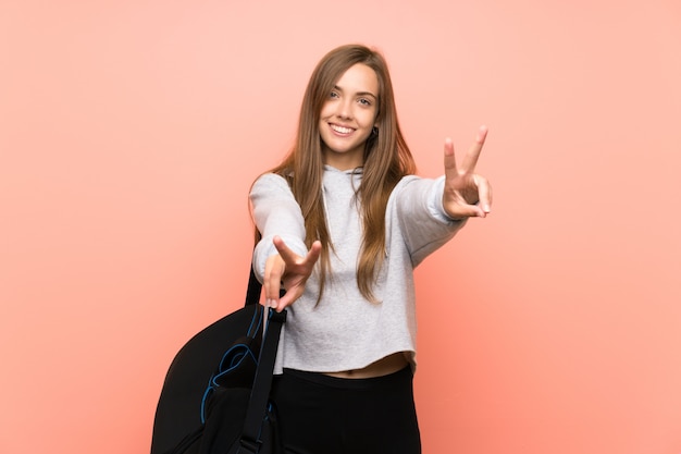 Young sport woman isolated pink  smiling and showing victory sign