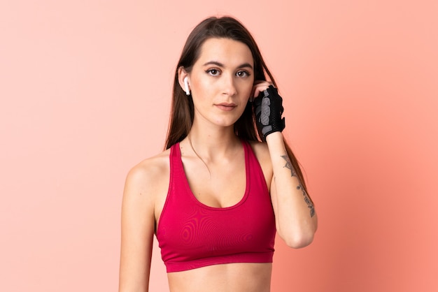 Young sport woman over isolated pink wall listening music