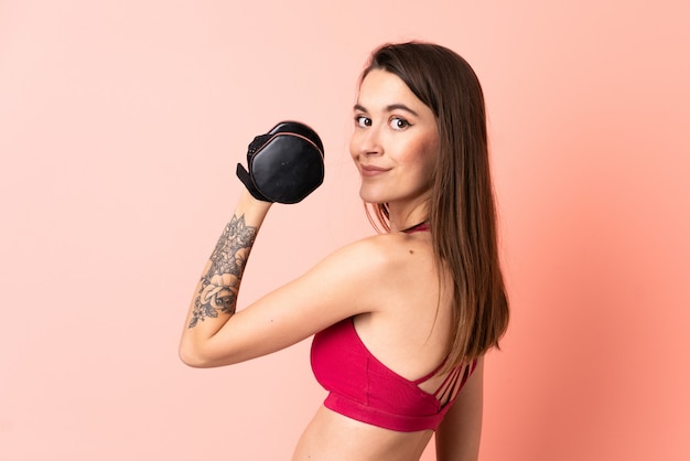 Young sport woman over isolated pink wall making weightlifting