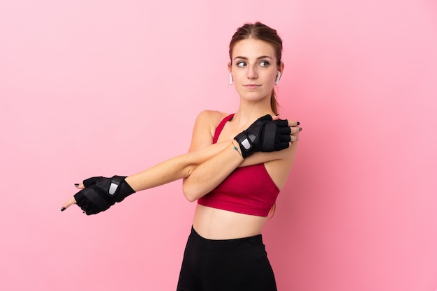 Young sport woman over isolated pink wall stretching arm