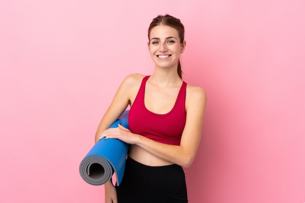 マットと笑顔で孤立したピンクの壁の上の若いスポーツ女性