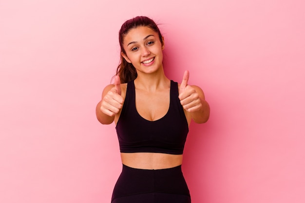 Young sport woman isolated on pink wall with thumbs ups, cheers about something