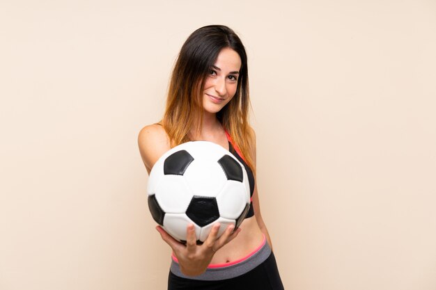 Young sport woman over isolated wall holding a soccer ball