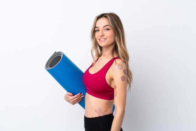 Young sport woman over isolated white wall with a mat and smiling