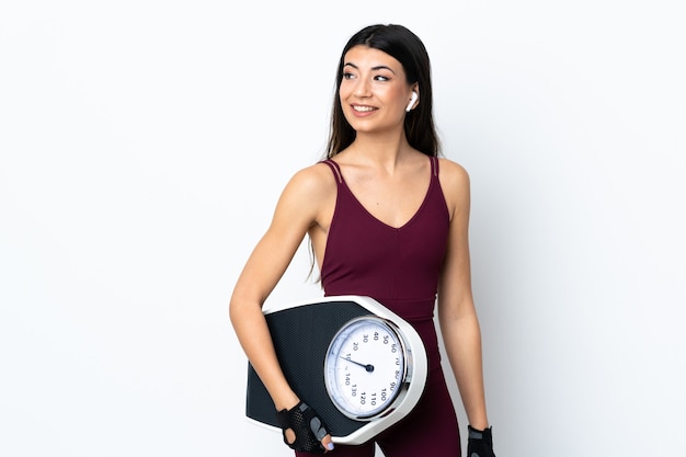Young sport woman over isolated white wall with weighing machine