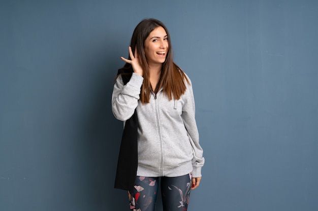 Foto giovane donna di sport che ascolta qualcosa mettendo la mano sull'orecchio