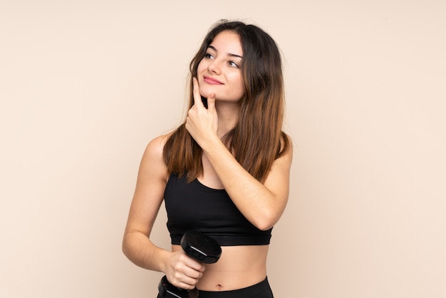 Young sport woman making weightlifting on beige thinking an idea