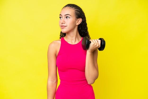 Young sport woman making weightlifting isolated on yellow background looking to the side