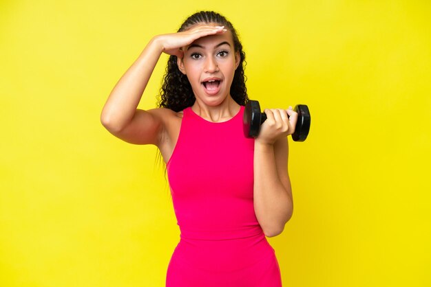 Young sport woman making weightlifting isolated on yellow background with surprise expression
