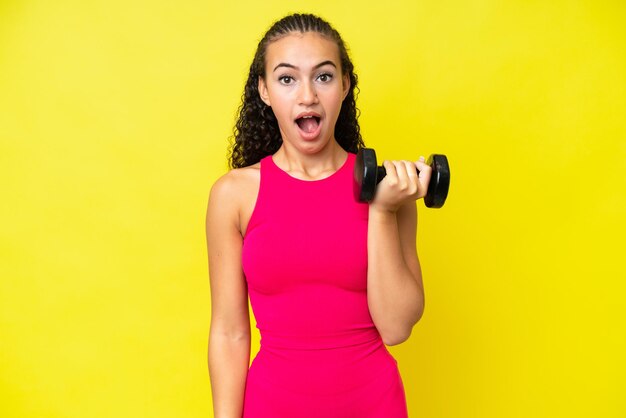 Young sport woman making weightlifting isolated on yellow background with surprise facial expression