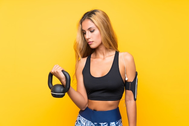 Young sport woman making weightlifting with kettlebell over isolated yellow wall