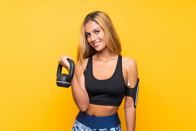 Young sport woman making weightlifting with kettlebell over isolated yellow