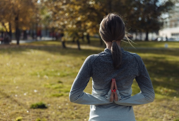 Giovane donna sportiva a praticare yoga namaste da dietro nel parco