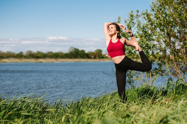 Giovane donna sportiva che pratica yoga all'aperto in riva al lago