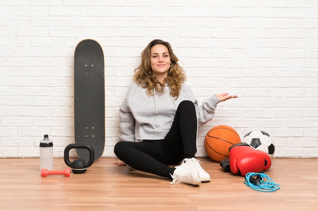 Young sport woman sitting on the floor holding copyspace imaginary on the palm
