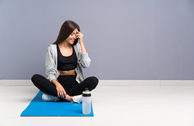 Young sport woman sitting on the floor with mat laughing