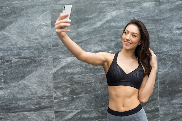 La giovane donna sportiva prende selfie dopo lo sport contro la parete di colore all'aperto