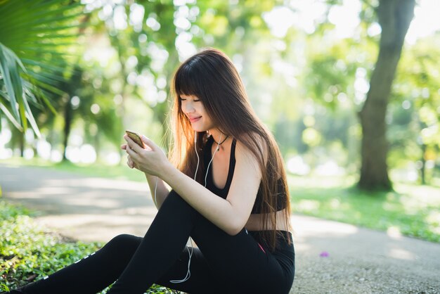 若いスポーツの女性は、公園でモバイルを使用して