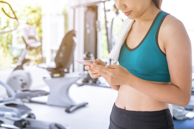 Giovane donna di sport che utilizza smart phone nella palestra, forma fisica, addestramento del concetto di stile di vita