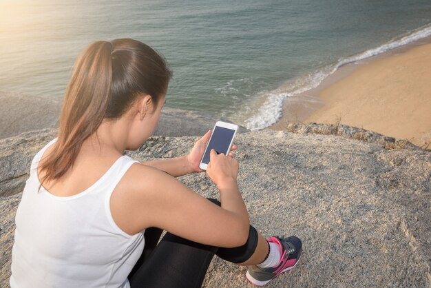 ビーチと海でスマートフォンを使用して若いスポーツの女性は背景です