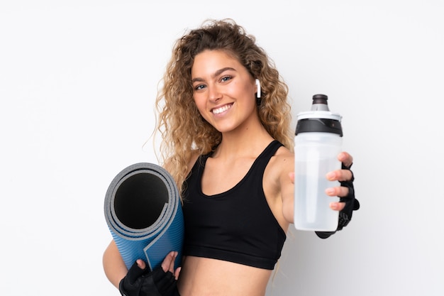 Young sport woman on white wall with sports water bottle and with a mat