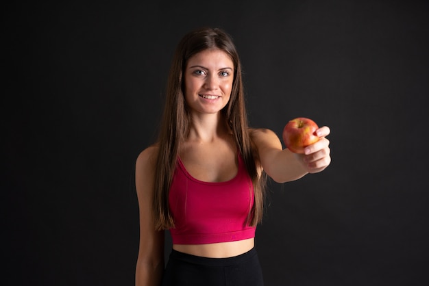 Young sport woman with an apple over isolated black 