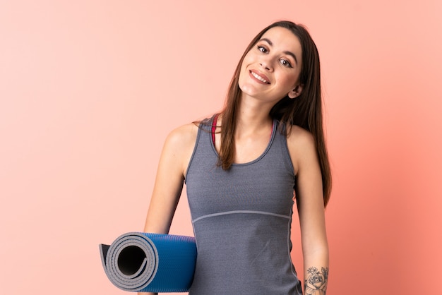 Young sport woman with mat over wall pointing to the side to present a product