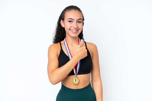 Молодая спортивная женщина с медалями на белом фоне показывает большой палец вверх
