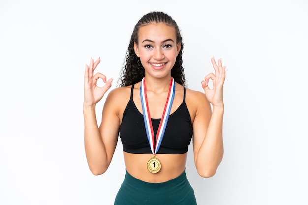 Молодая спортивная женщина с медалями на белом фоне показывает пальцами знак "ок"