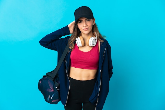 Young sport woman with sport bag isolated on blue background having doubts