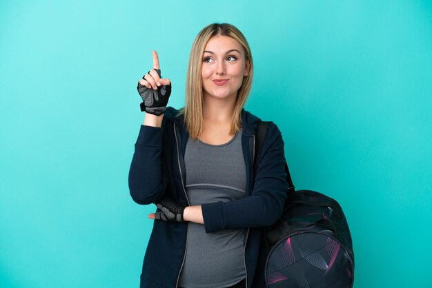 Young sport woman with sport bag isolated on blue background pointing up a great idea