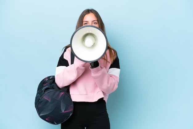 Foto giovane donna sportiva con borsa sportiva isolata su sfondo blu che grida attraverso un megafono