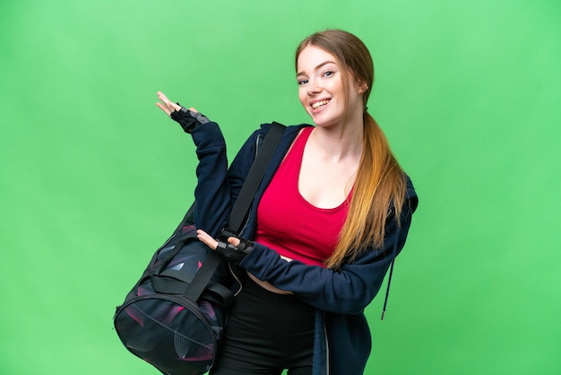 Young sport woman with sport bag over isolated chroma key background extending hands to the side for inviting to come