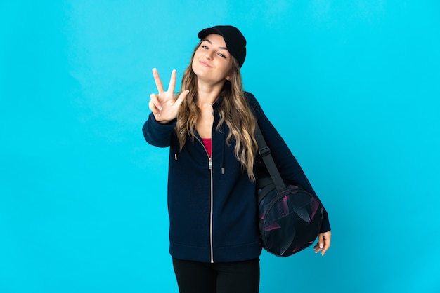 Young sport woman with sport bag isolated happy and counting three with fingers
