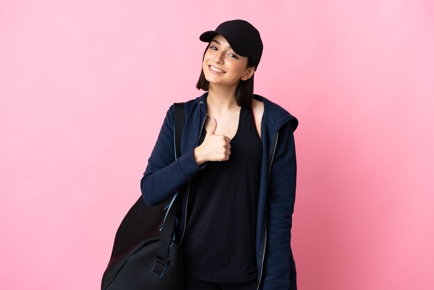 Young sport woman with sport bag isolated on pink background giving a thumbs up gesture