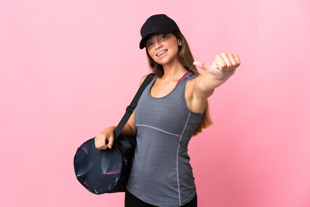 Young sport woman with sport bag isolated on pink giving a thumbs up gesture