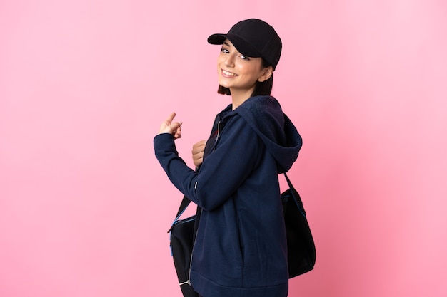 Young sport woman with sport bag isolated on pink pointing back