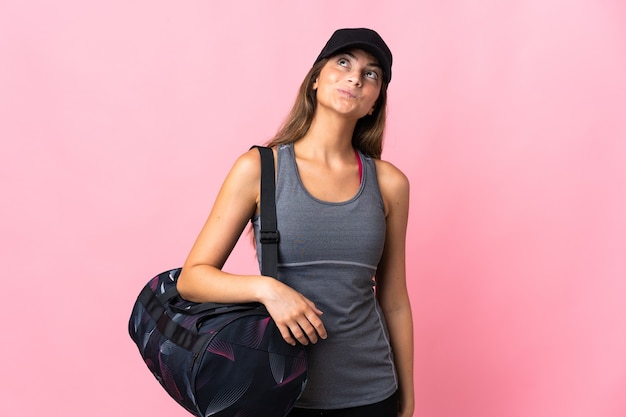 Young sport woman with sport bag isolated on pink wall and looking up