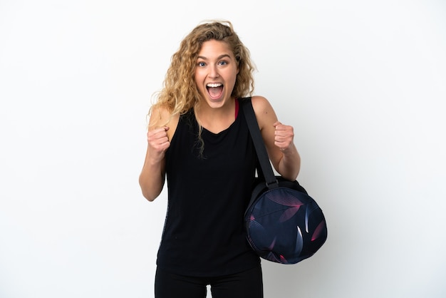 Young sport woman with sport bag isolated on white background celebrating a victory in winner position