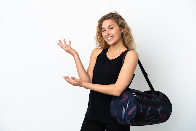 Young sport woman with sport bag isolated on white background extending hands to the side for inviting to come