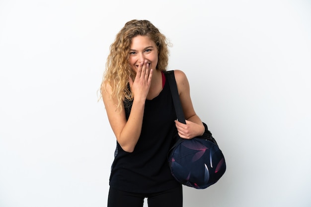 白い背景で隔離のスポーツバッグを持つ若いスポーツ女性幸せと笑顔の手で口を覆う