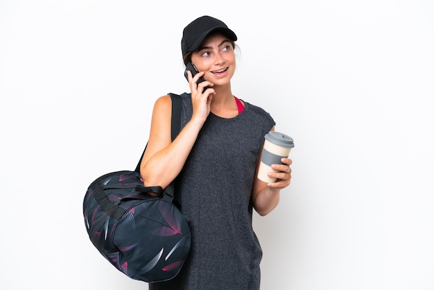 Young sport woman with sport bag isolated on white background holding coffee to take away and a mobile