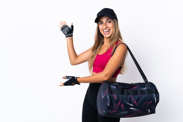 Young sport woman with sport bag over isolated white wall extending hands to the side for inviting to come