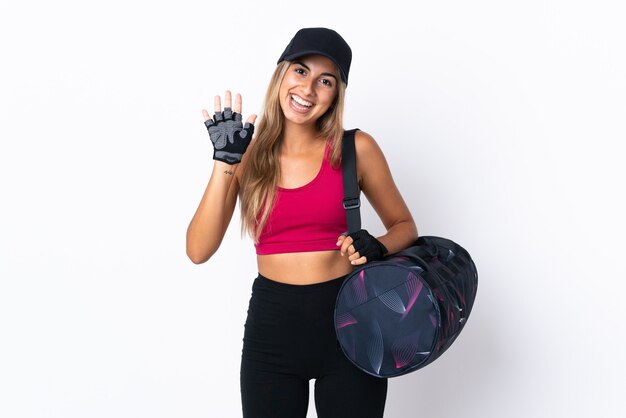 Young sport woman with sport bag over isolated white wall saluting with hand with happy expression