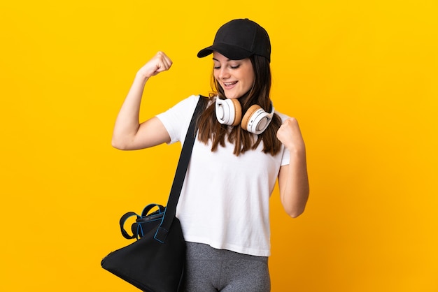 Young sport woman with sport bag isolated on yellow celebrating a victory