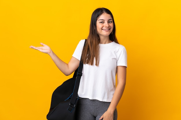 Young sport woman with sport bag isolated on yellow extending hands to the side for inviting to come