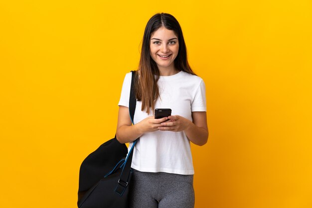 Young sport woman with sport bag isolated on yellow surprised and sending a message