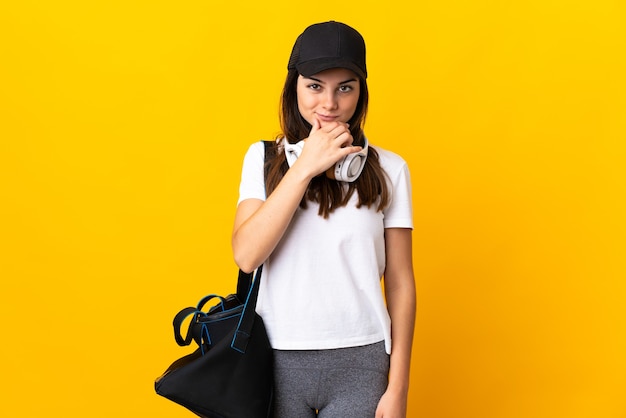 Young sport woman with sport bag isolated on yellow wall thinking