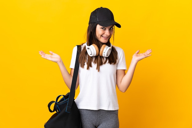 Young sport woman with sport bag isolated on yellow wall with shocked facial expression